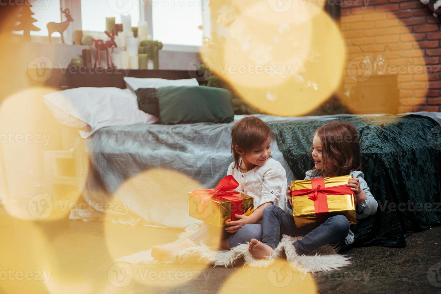 gelukkige kinderen. kerstvakantie met cadeaus voor deze twee kinderen die binnen zitten in de mooie kamer bij het bed foto