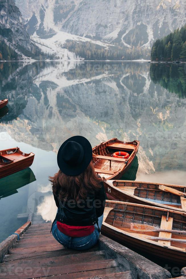 vrouw in zwarte hoed genietend van majestueus berglandschap in de buurt van het meer met boten foto