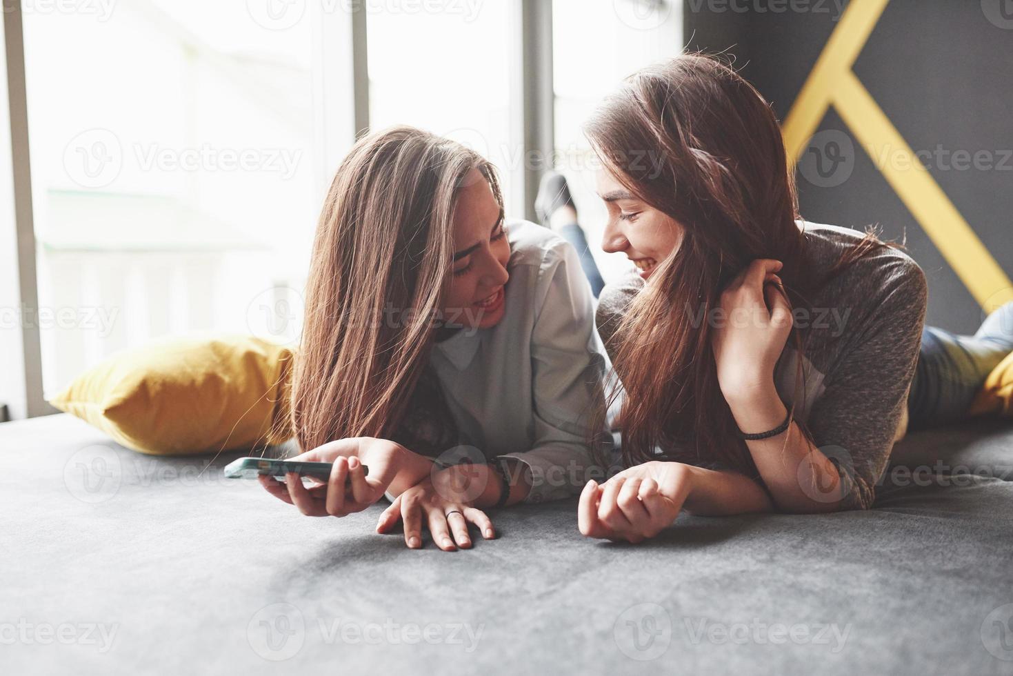 twee schattige lachende tweelingzusjes die smartphone vasthouden en selfie maken. meisjes liggen op de bank poseren en vreugde foto