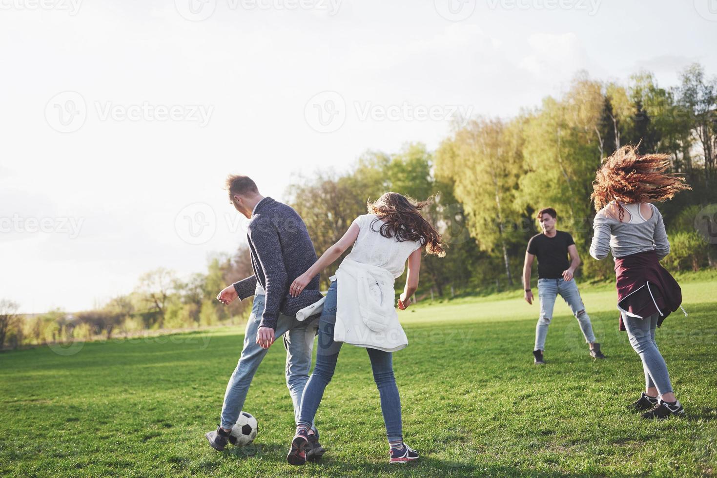 een groep vrienden in casual outfit voetballen in de open lucht. mensen veel plezier en plezier. actieve rust en schilderachtige zonsondergang foto