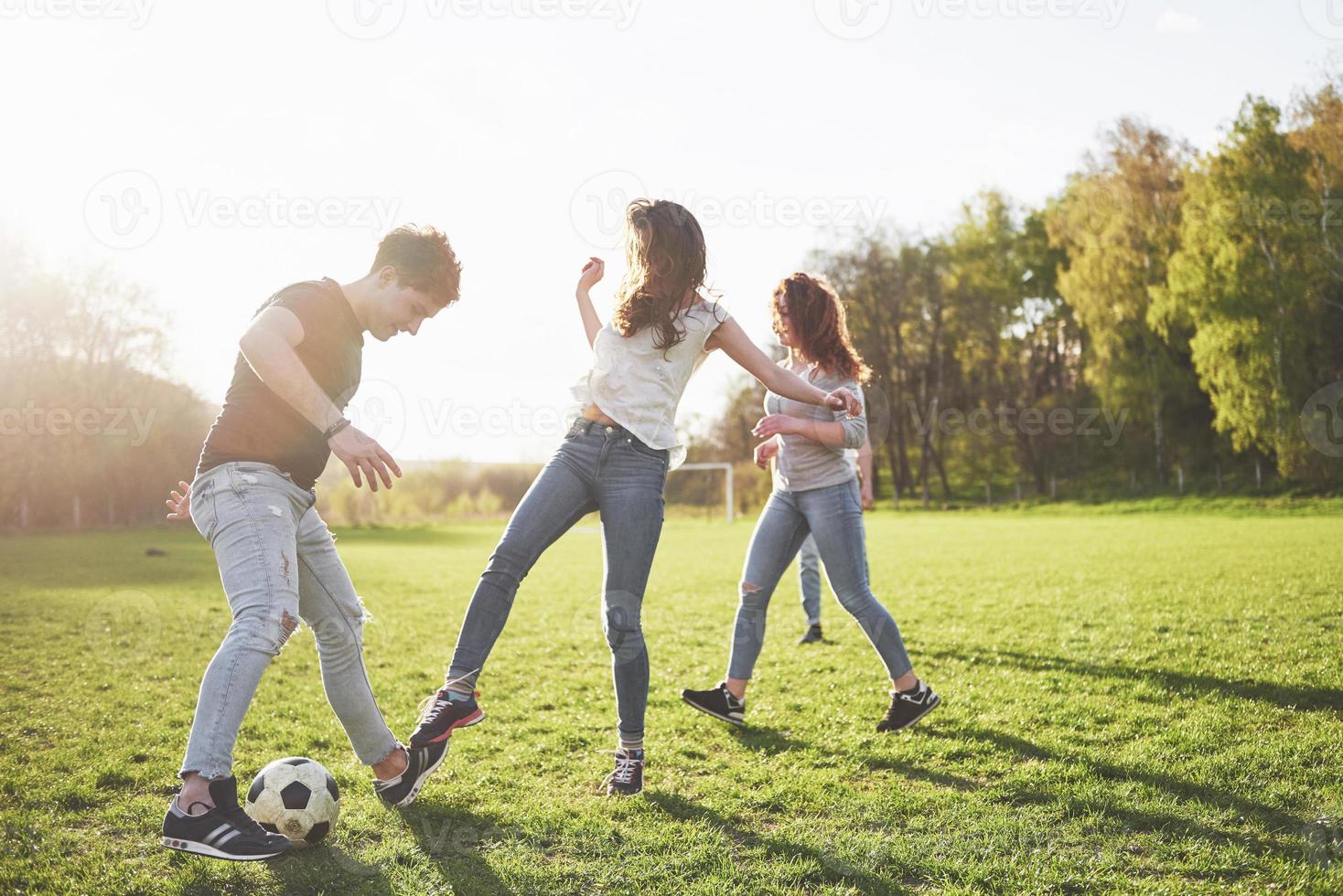 een groep vrienden in casual outfit voetballen in de open lucht. mensen veel plezier en plezier. actieve rust en schilderachtige zonsondergang foto