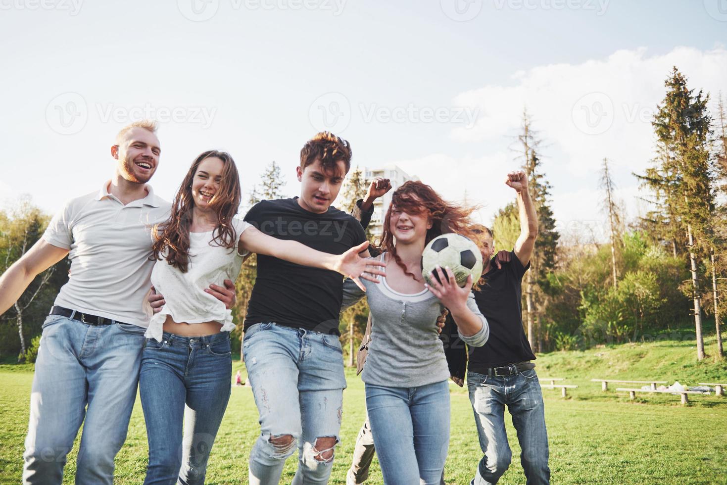 een groep vrienden in casual outfit voetballen in de open lucht. mensen veel plezier en plezier. actieve rust en schilderachtige zonsondergang foto