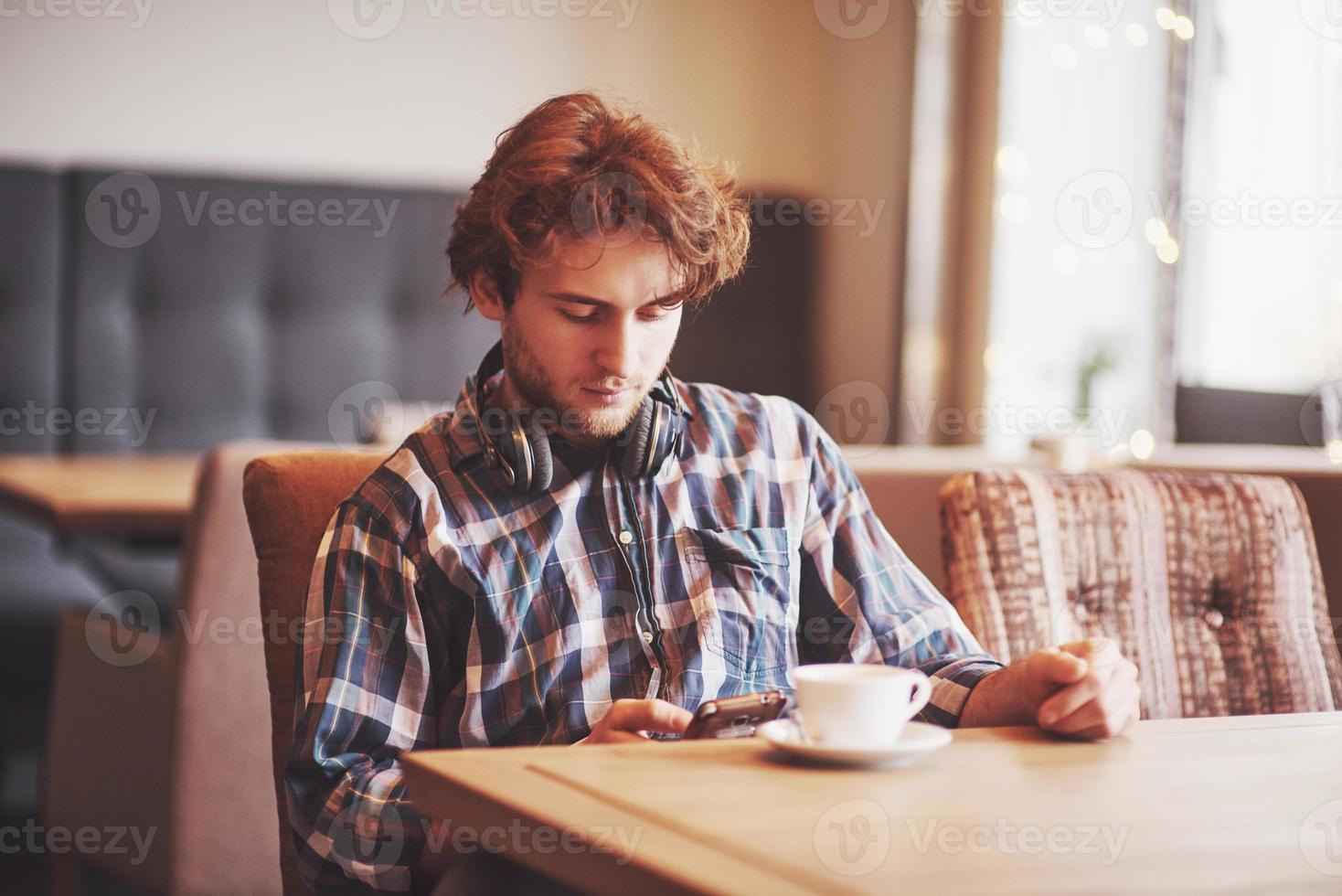 jonge man freelancer met een baard in alledaagse kleding zittend in een café met een kopje koffie foto