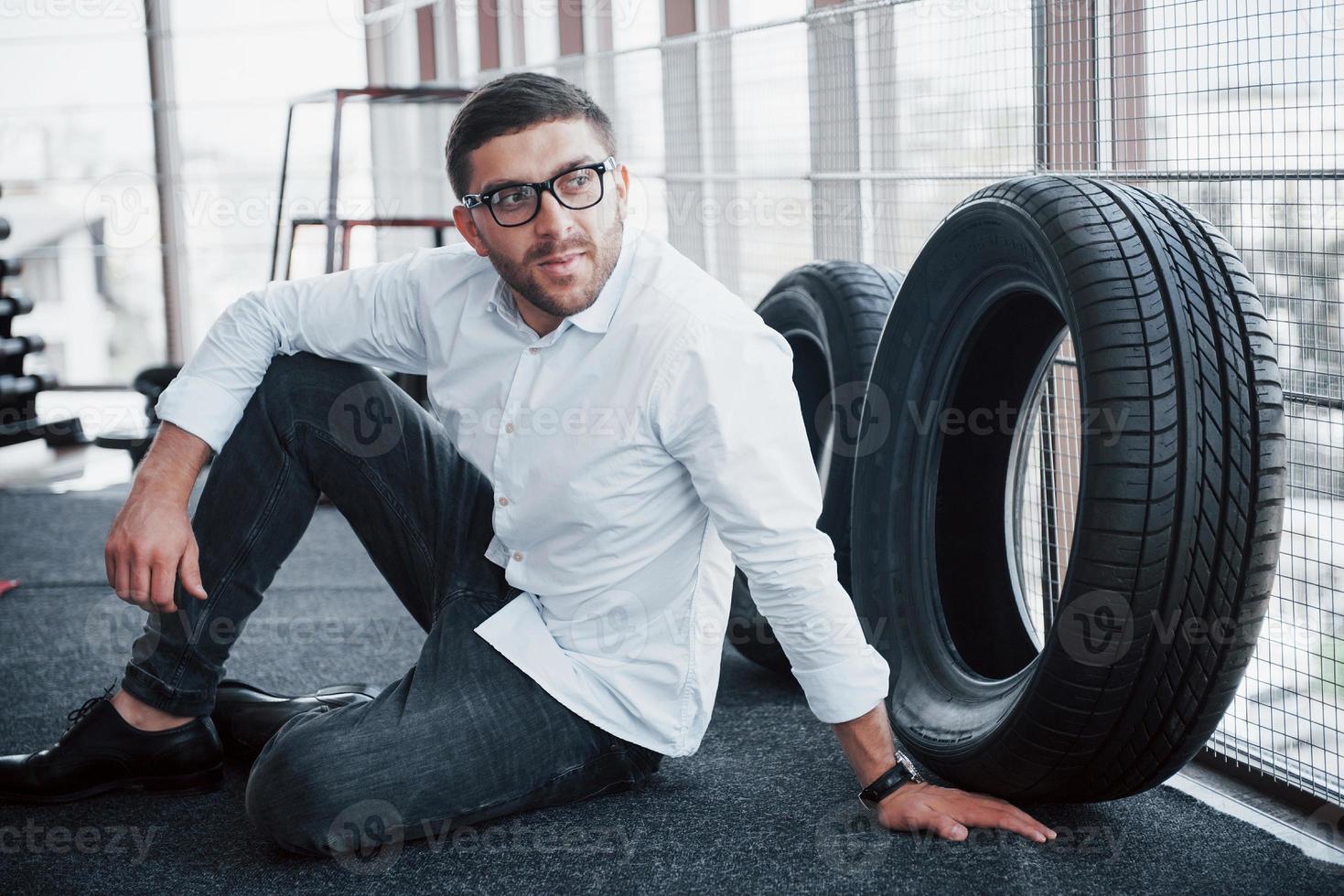 een knappe jongen zittend op de vloer in de sportschool, in een wit shirt en broek. concept van sport foto