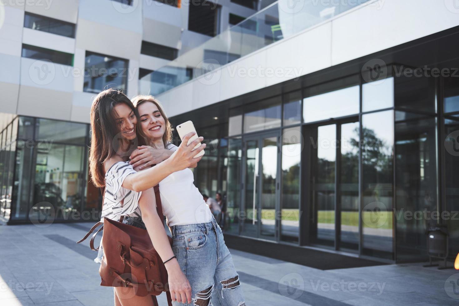 twee mooie gelukkige jonge student meisje met rugzak in de buurt van de campus van de universiteit en selfie foto maken. onderwijs en vrije tijd concept
