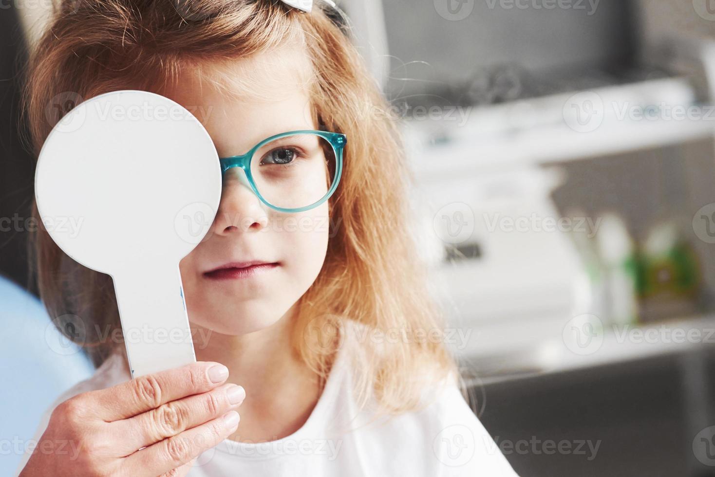 probeer dat woord eens te lezen. vrouw handen houdt de occluder. klein meisje dat zijn zicht controleert met een nieuwe groene bril foto