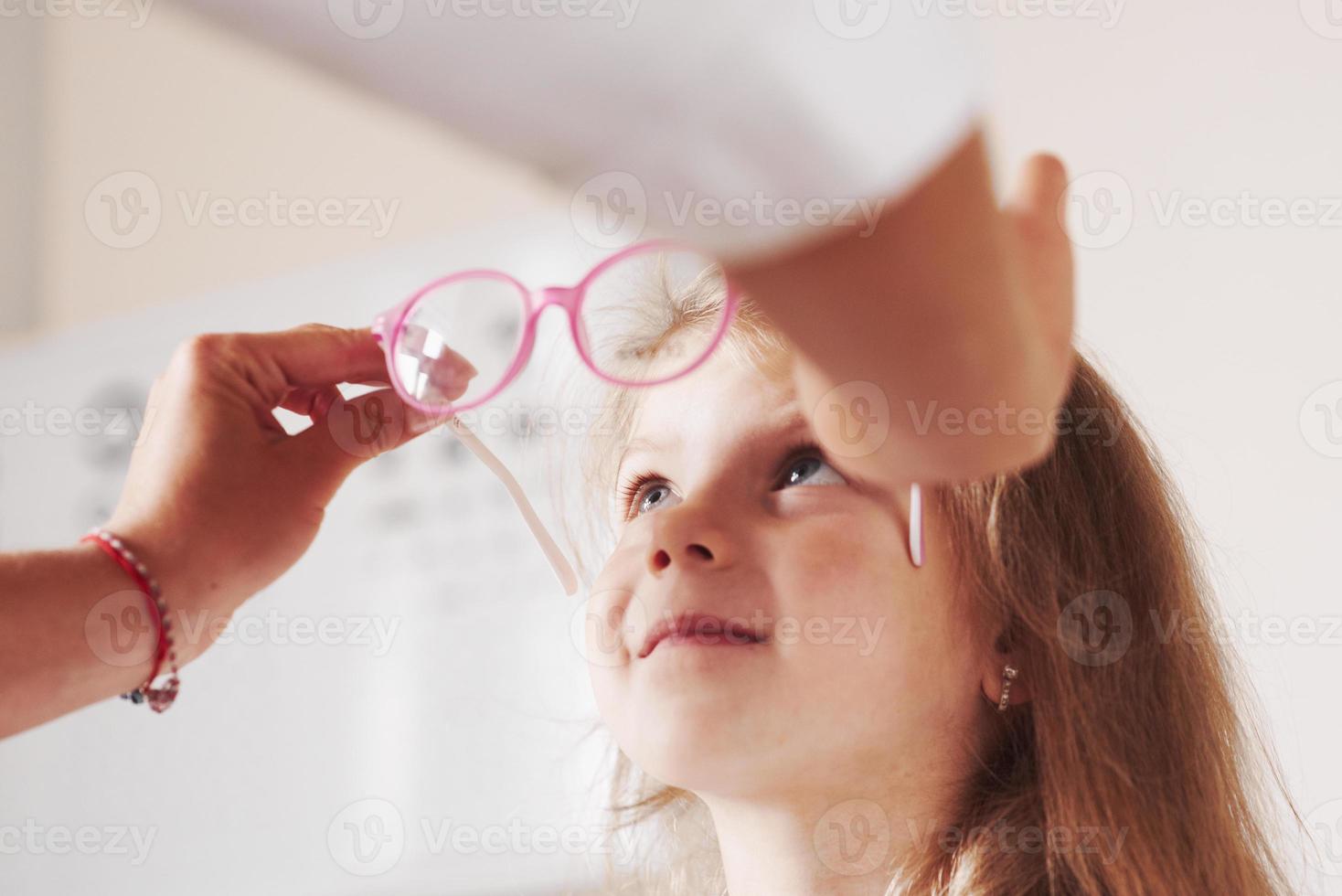 voelt zich opgewonden. dokter geeft het kind een nieuwe roze bril voor zijn zicht foto