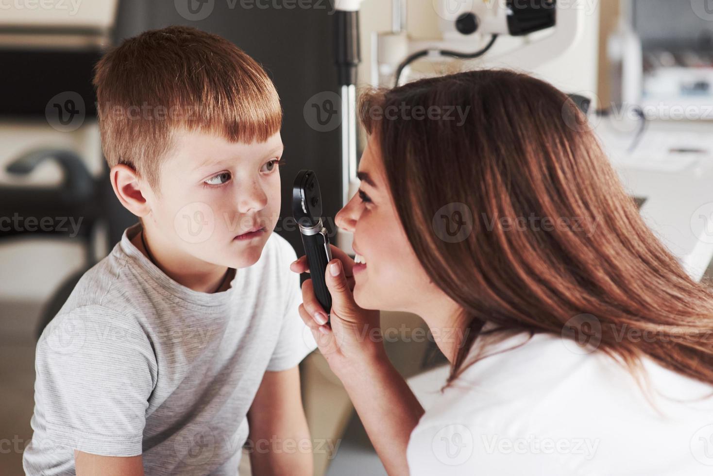 vrouw bezig met het controleren van de ogen van het jonge kind en glimlacht tijdens het proces foto