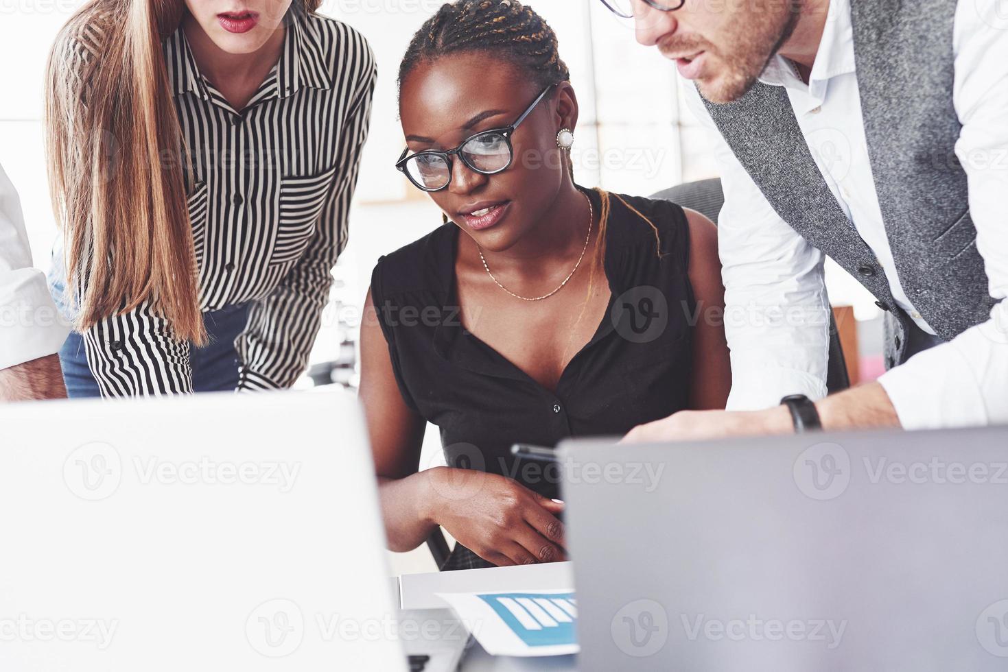 Afro-Amerikaanse vrouw die met teamgenoten naar de laptop kijkt. zakelijke en kantoorconceptie foto