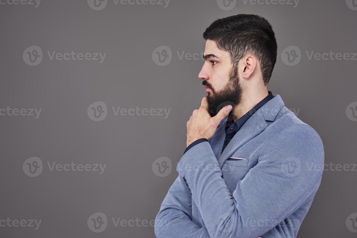 portret van freelancer man met baard in jas staande tegen een grijze achtergrond foto