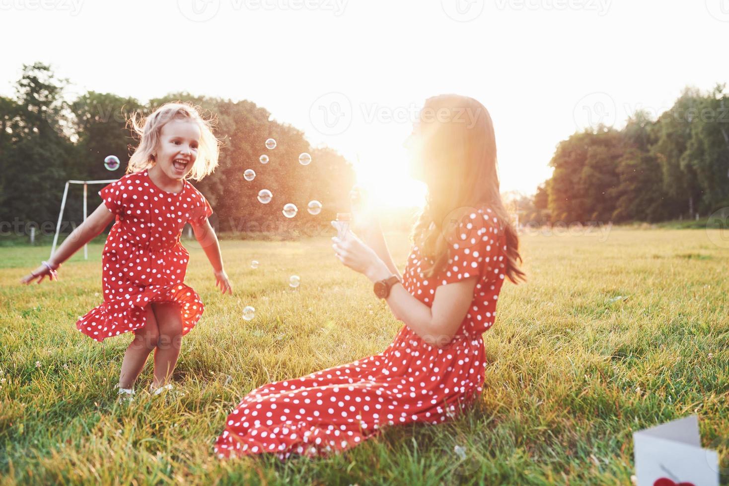 probeer ze te vangen. meisje met haar dochter die plezier heeft met bubbels buiten zittend op het gras foto