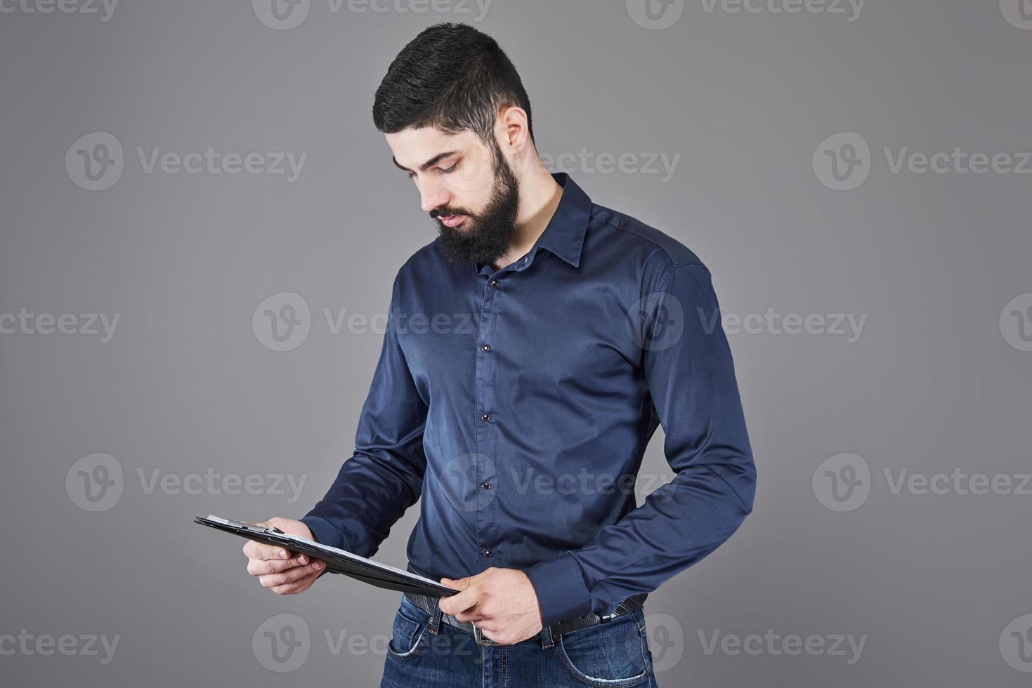 geconcentreerde jonge aantrekkelijke zakenman in blauw shirt plannen en schrijven in klembord foto