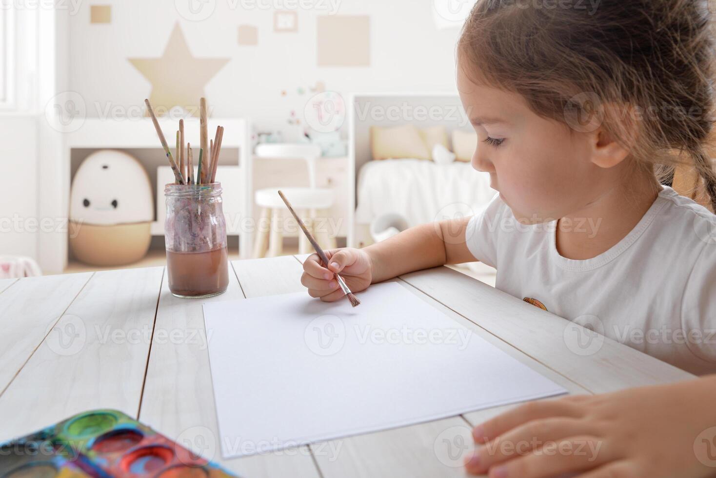 jong meisje schilderij met aquarellen Aan wit papier in haar kamer. ideaal voor kinderen creativiteit of artistiek concepten foto