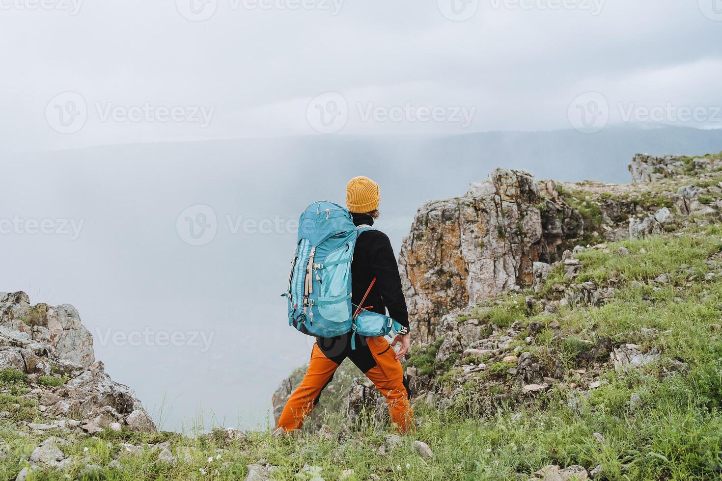 trekking Aan voet in de bergen met een rugzak, achterzijde visie van een persoon in de bergen, een wandelen in natuur, een zomer vakantie zonder sociaal netwerken, eenzaamheid in stilte. foto