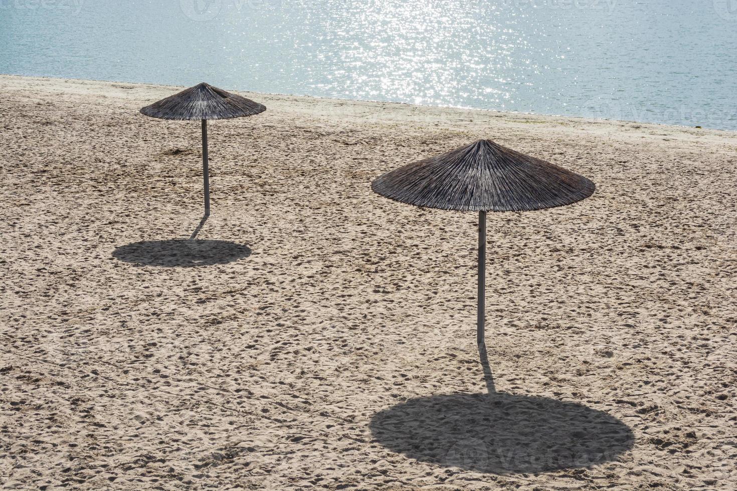 twee eenzame rieten parasols op een leeg strand 's middags onder de zon foto