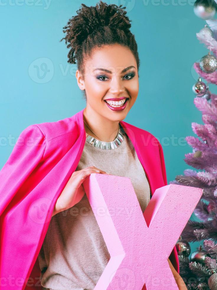 gelukkige en vrolijke afro-amerikaanse vrouw met huidige doos op de achtergrond van de kerstboom. kerstmis, nieuwjaar, geluk, vakantieconcept foto