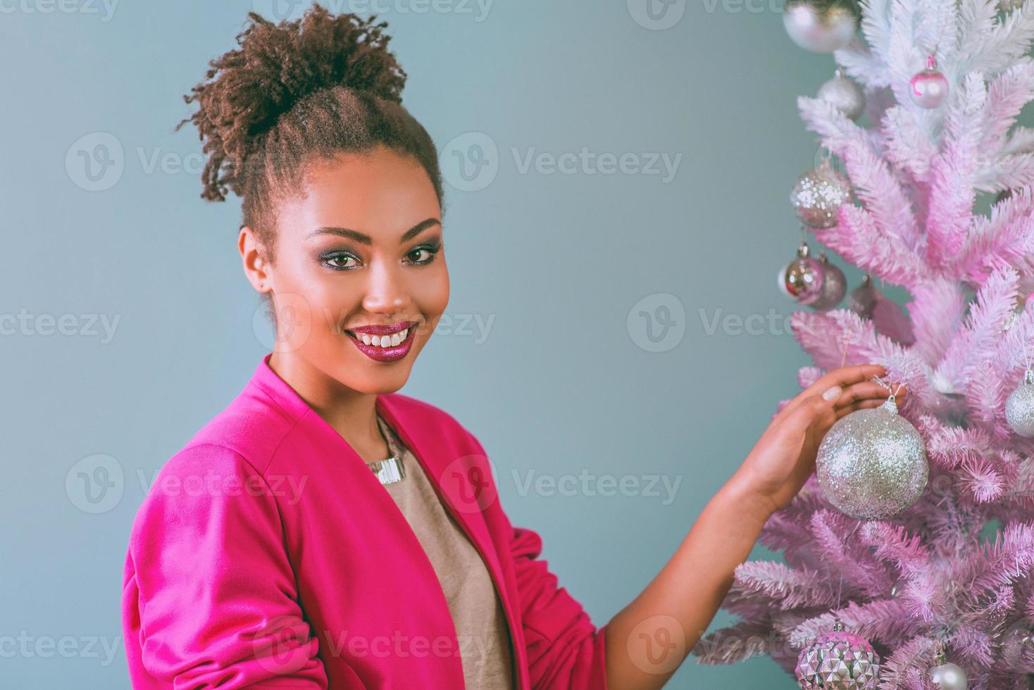 gelukkige en vrolijke afro-amerikaanse vrouw met huidige doos op de achtergrond van de kerstboom. kerstmis, nieuwjaar, geluk, vakantieconcept foto