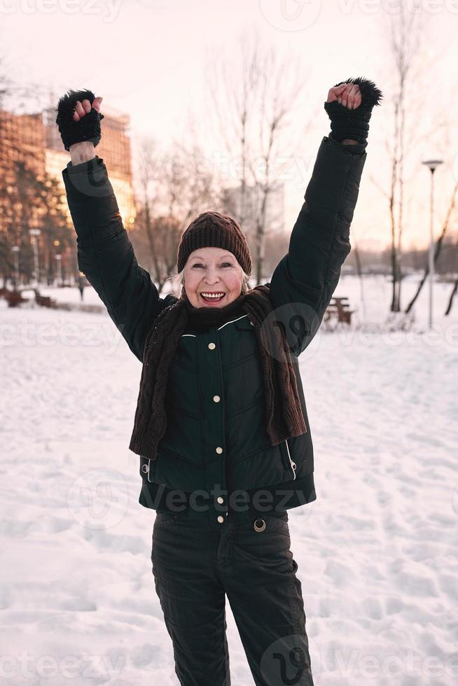 senior vrouw in hoed en sportieve jas die sportoefeningen doet in het sneeuwwinterpark. winter, leeftijd, sport, activiteit, seizoensconcept foto