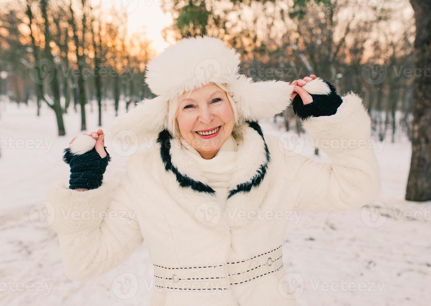 senior vrouw in witte hoed en bontjas genieten van de winter in het sneeuwbos. winter, leeftijd, seizoen concept foto