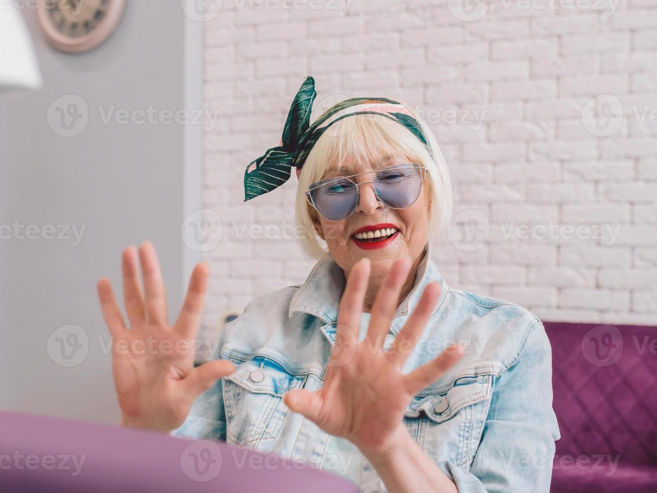 manicure meester in blauwe handschoenen afroming handen van oudere stijlvolle vrouw in blauwe zonnebril en spijkerjasje zittend op manicure salon foto