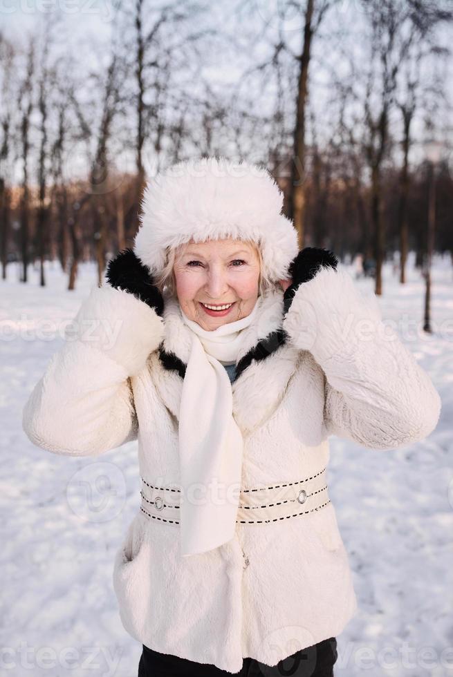 senior vrouw in witte hoed en bontjas genieten van de winter in het sneeuwbos. winter, leeftijd, seizoen concept foto