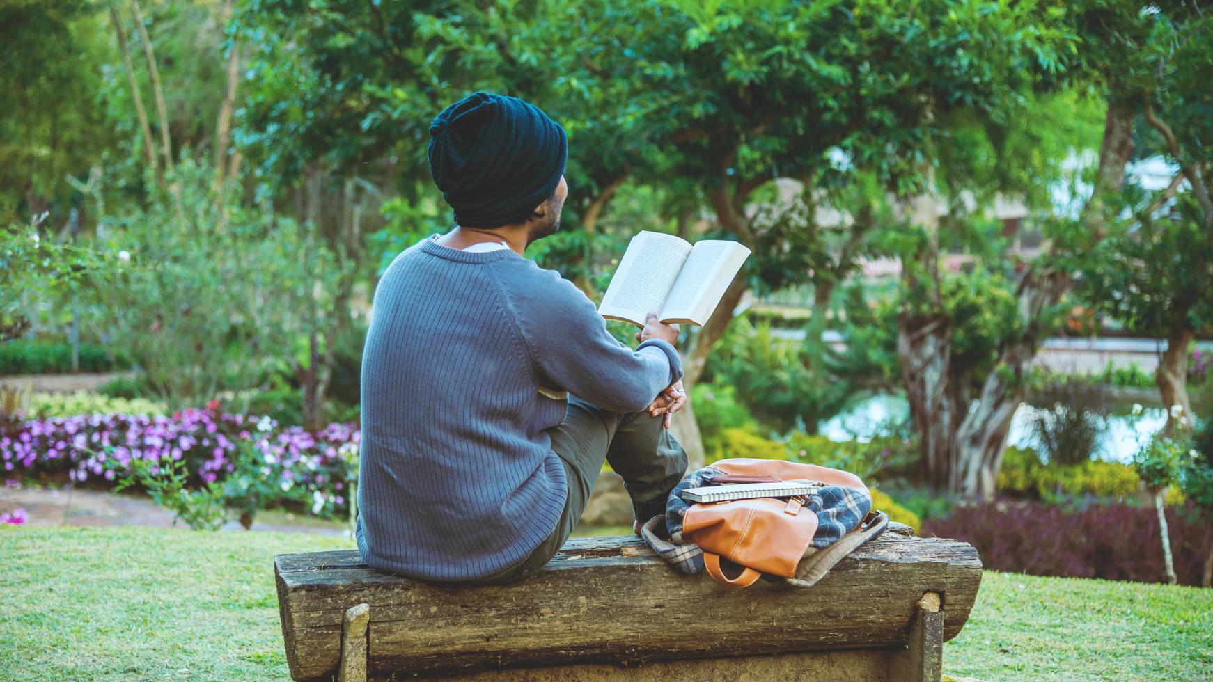 de jonge man was een boek aan het lezen in het park. tussen de natuurlijke bomen en de prachtige bloementuin foto