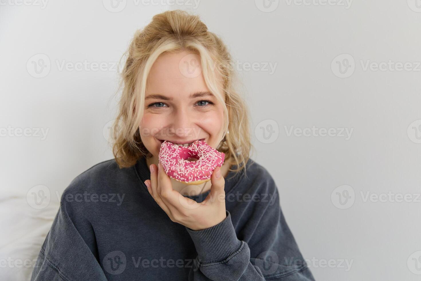 portret van schattig blond meisje Holding roze donut met hagelslag Aan bovenkant, tonen haar favoriete voedsel foto