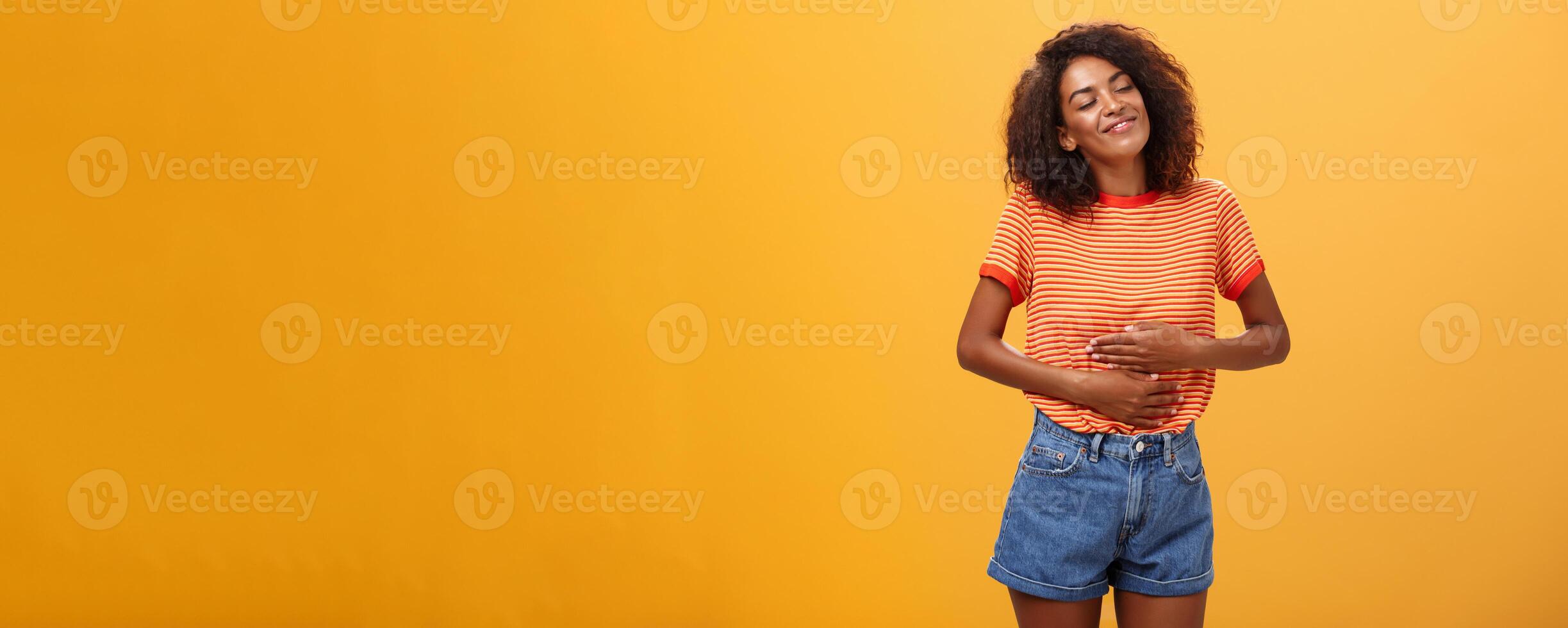 mmm heerlijk maaltijd opwarming me binnen. verheugd gevuld mooi elegant jong vrouw in gestreept t-shirt wrijven buik met tevredenheid sluitend ogen van genoegen na aan het eten smakelijk voedsel foto