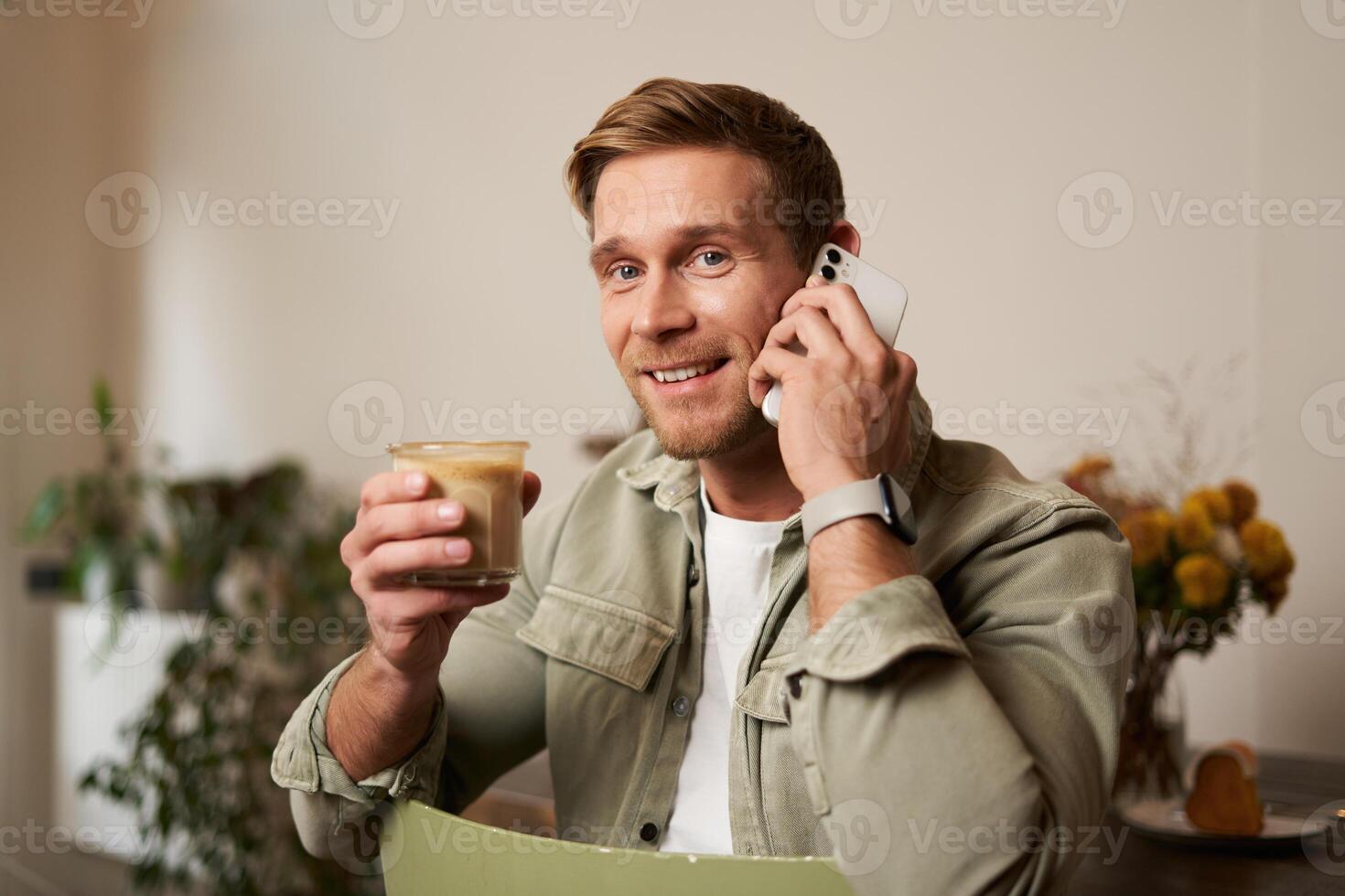 beeld van lachend, mooi jong blond Mens met telefoon, drinken koffie in cafe, pratend naar iemand over- de telefoon, beantwoorden een telefoontje foto