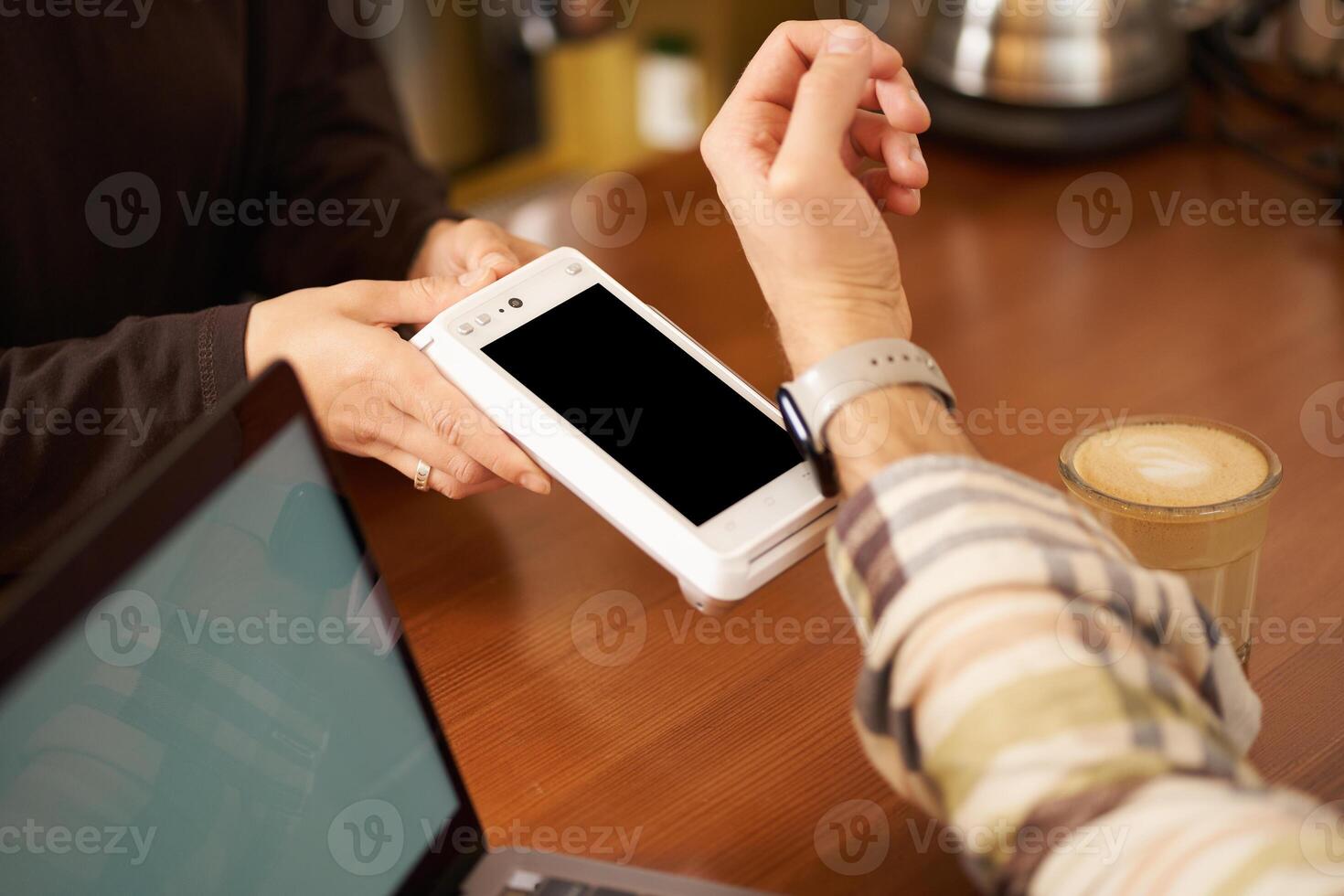 Mens in cafe betalen contactloos gebruik makend van zijn digitaal kijk maar Aan pols, Holding het dichtbij naar de pos contactloos terminal, werken van coworking foto