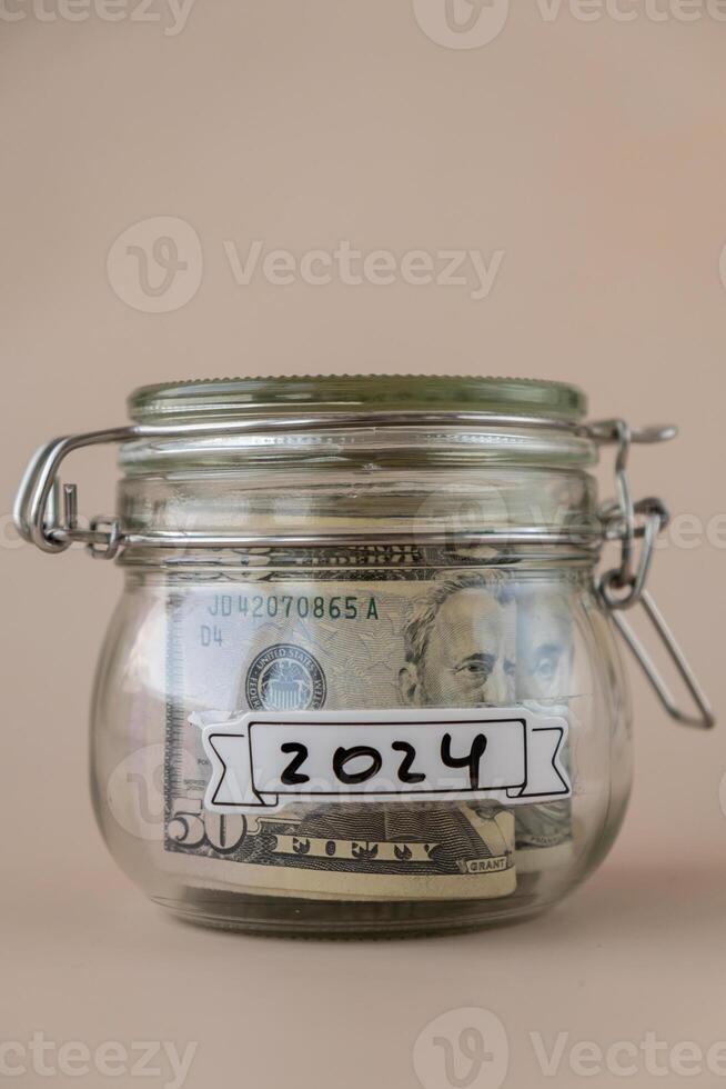 glas pot vol van Amerikaans valuta dollars contant geld bankbiljet met tekst 2024 jaar. voorbereiding besparing geld. matig consumptie en economie. verzamelen geld foto