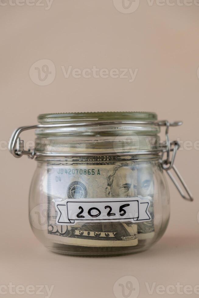 glas pot vol van Amerikaans valuta dollars contant geld bankbiljet met tekst 2025 jaar. voorbereiding besparing geld. matig consumptie en economie. verzamelen geld foto