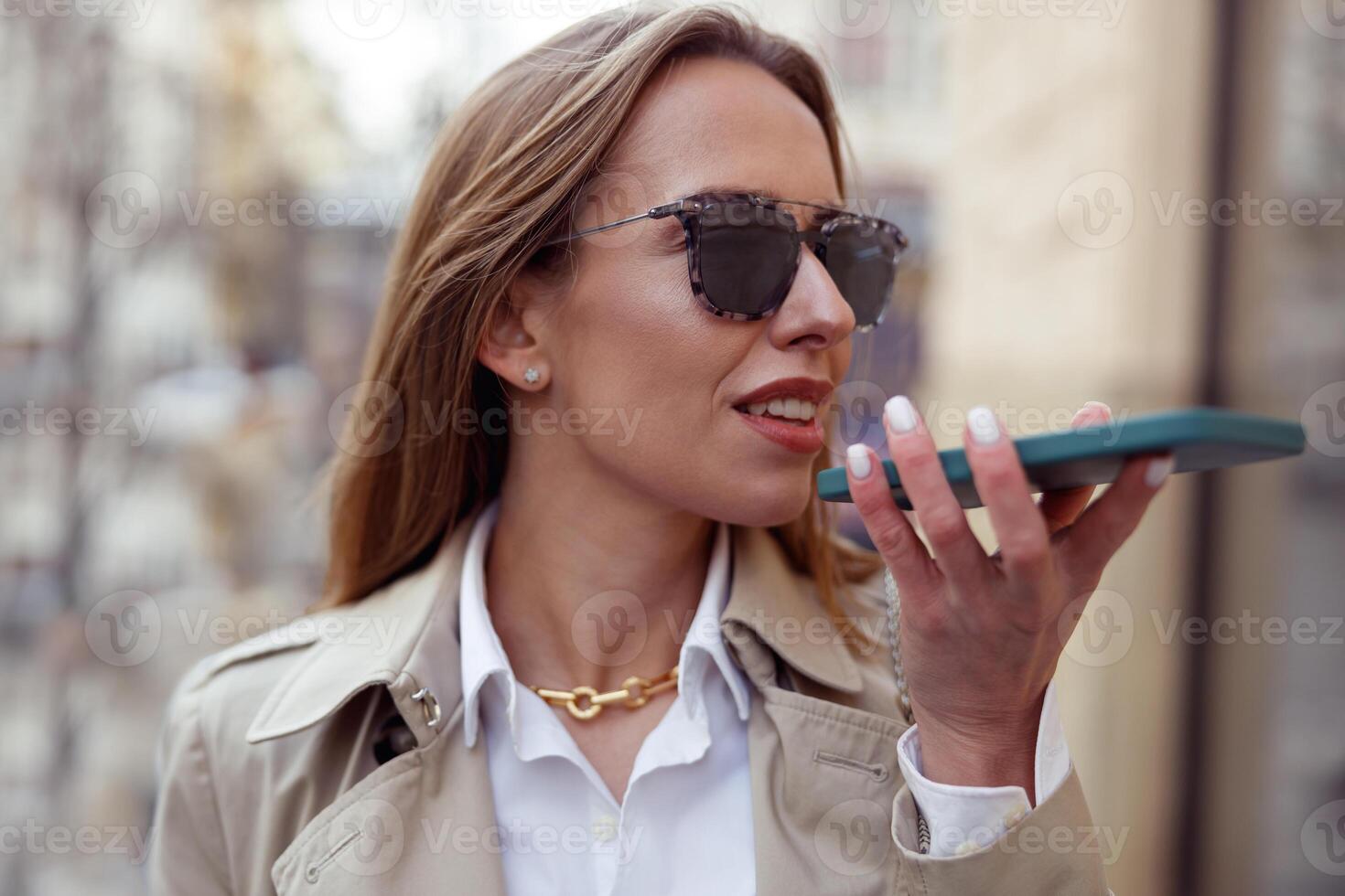 gelukkig zakenvrouw in zonnebril is opname audio bericht Aan telefoon Aan stad straat achtergrond foto