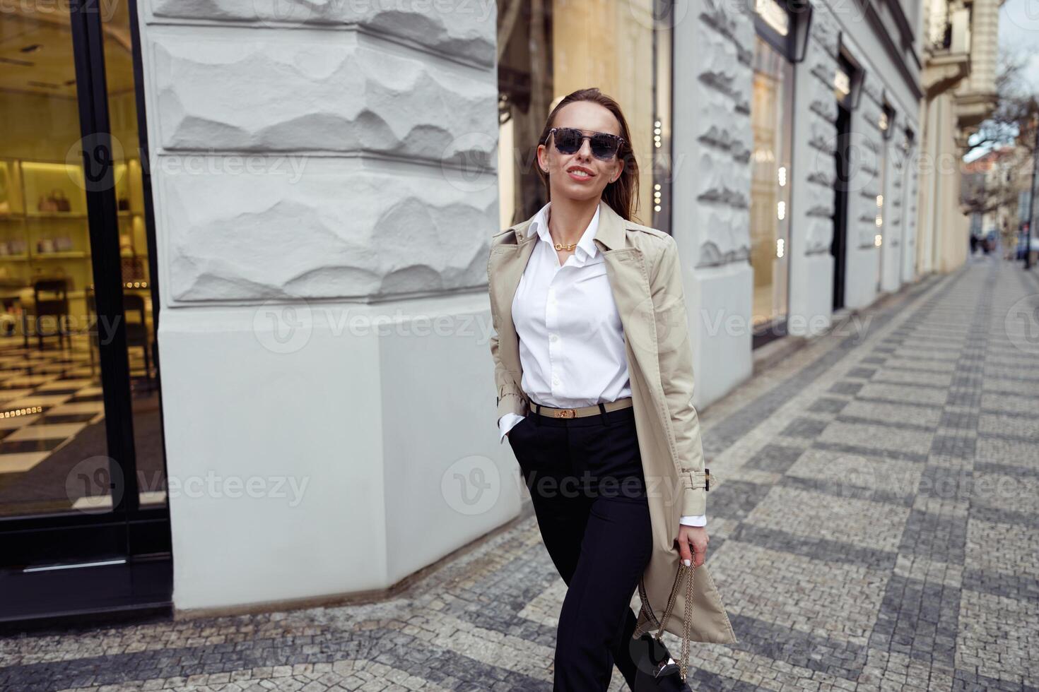 gelukkig modieus vrouw in zonnebril staand Aan stad straat achtergrond en op zoek Bij camera foto