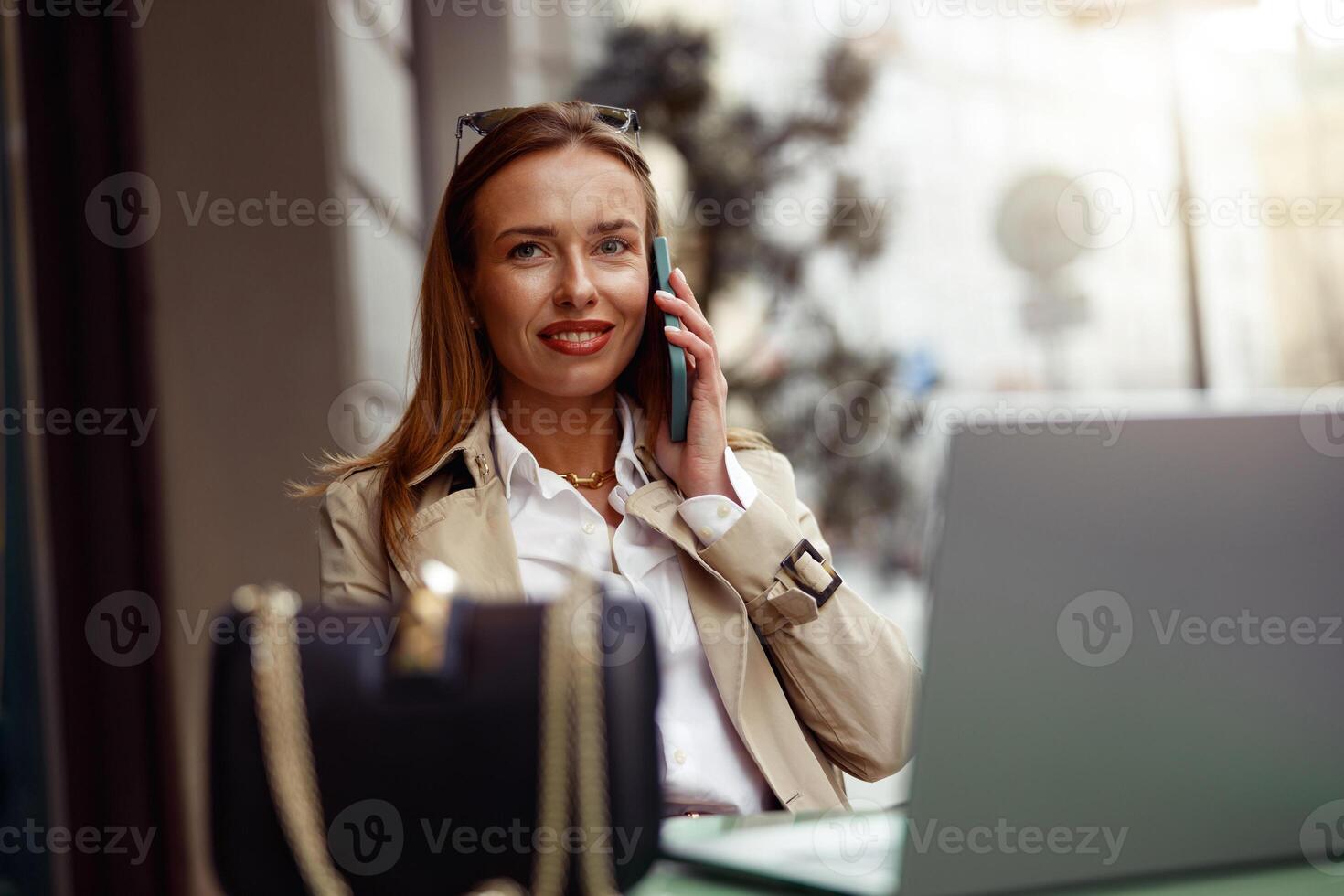 glimlachen Europese zakenvrouw pratend telefoon terwijl werken online zittend Bij buitenshuis cafe terras foto