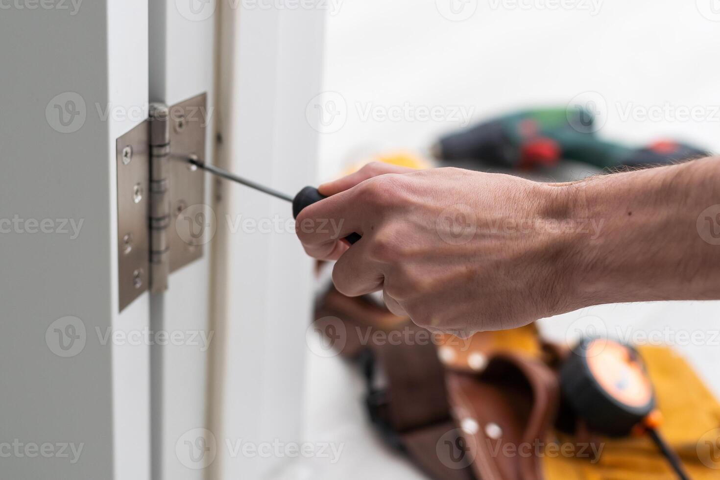 Mens verwijderen de deur. wendingen zelftappend schroef met een schroevendraaier. roestvrij deur scharnieren Aan een wit deur foto
