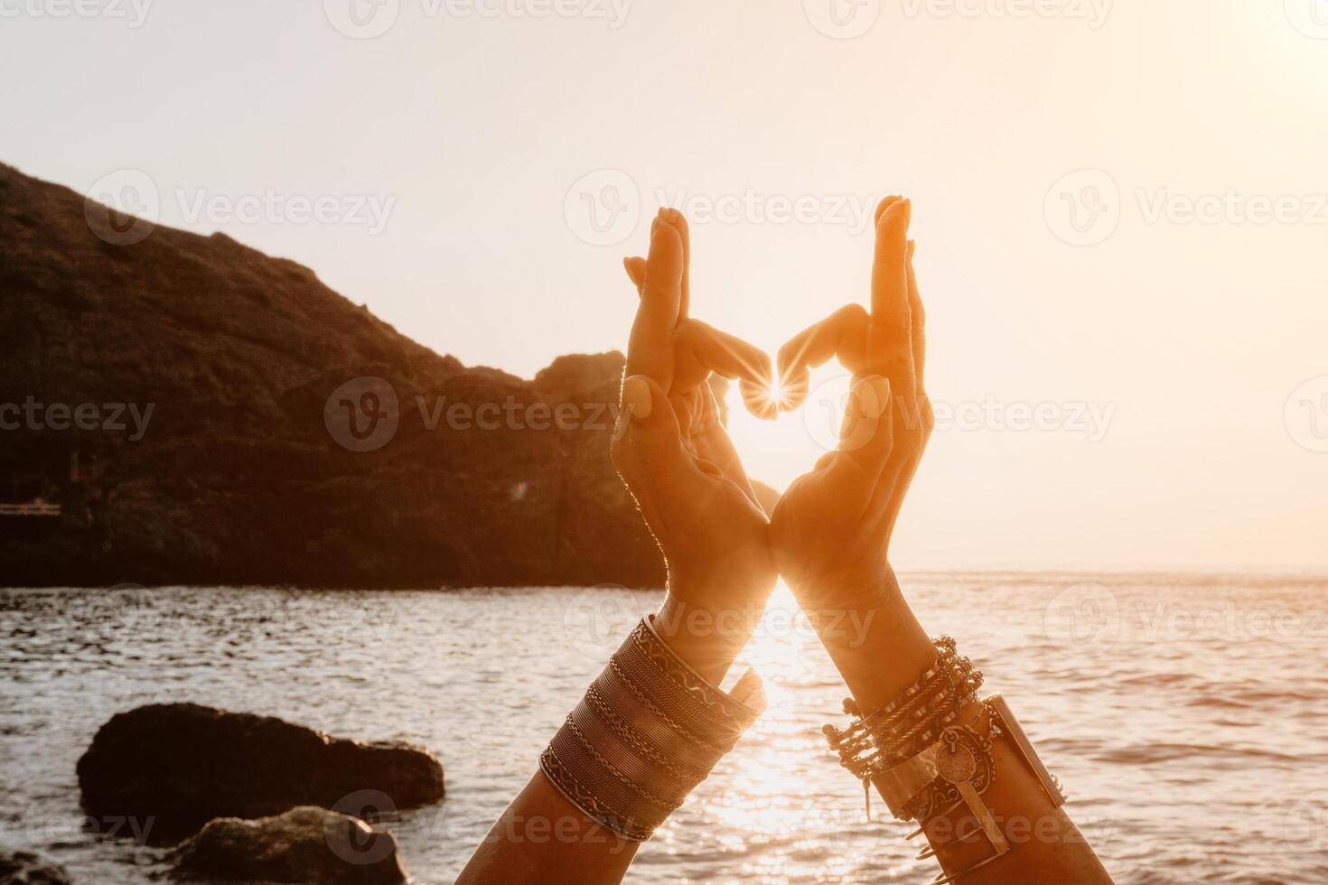 vrouw zee yoga. gelukkig vrouw in een wit zwempak en boho-stijl armbanden maken een hart vorm met haar handen terwijl beoefenen yoga Aan een mat door zee Bij zonsondergang. gezond levensstijl, harmonie en meditatie foto