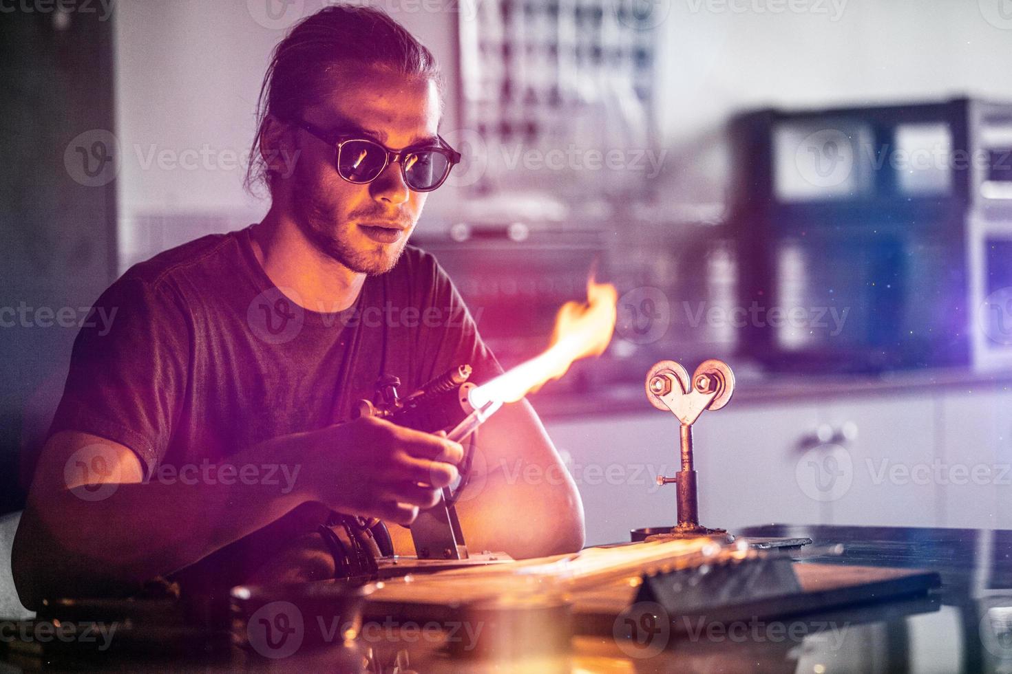 glasblazende jonge man aan het werk aan een fakkelvlam met glazen buizen foto