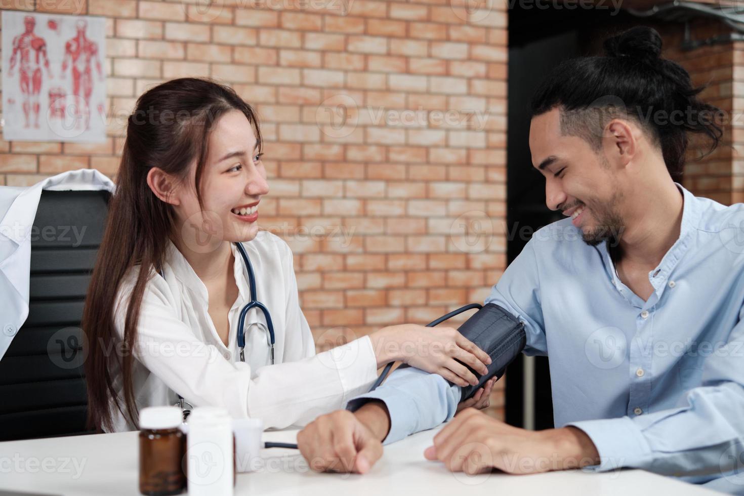 mooie vrouw arts in wit overhemd die Aziatische persoon met stethoscoop is gezondheid onderzoekt mannelijke patiënt in bakstenen muur achtergrond medische kliniek, glimlachend adviserend medisch specialist beroep. foto