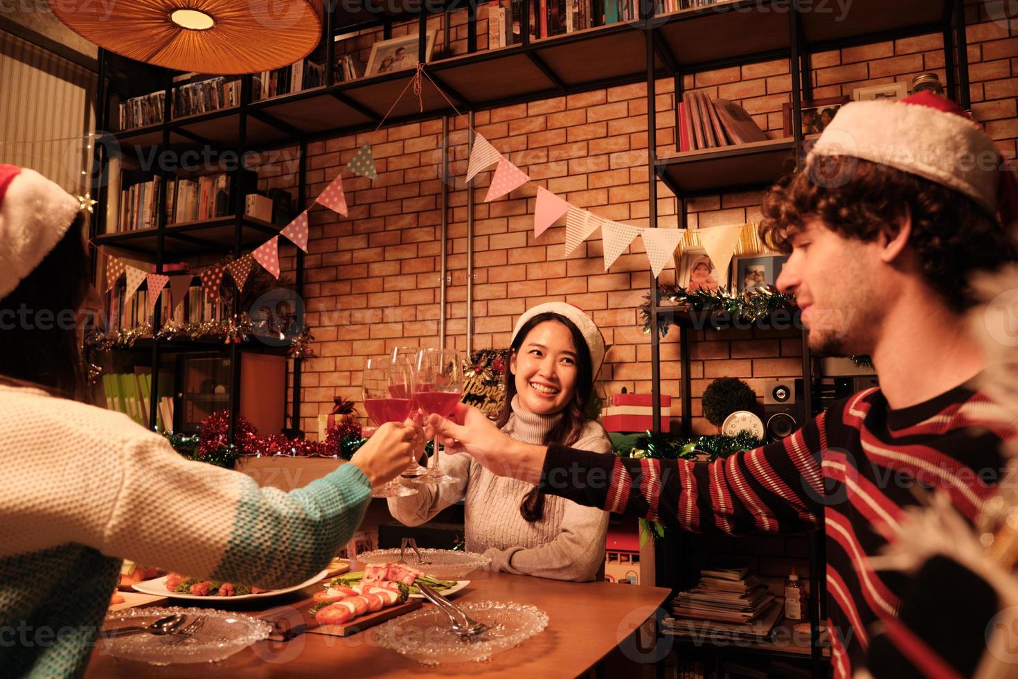 geluk familie en vrienden vieren, heffen een bril en een vrolijke glimlach met drankjes, genieten van het eten van voedsel in de eetkamer van het huis, ingericht voor kerstfestivalfeest en nieuwjaarsdag. foto