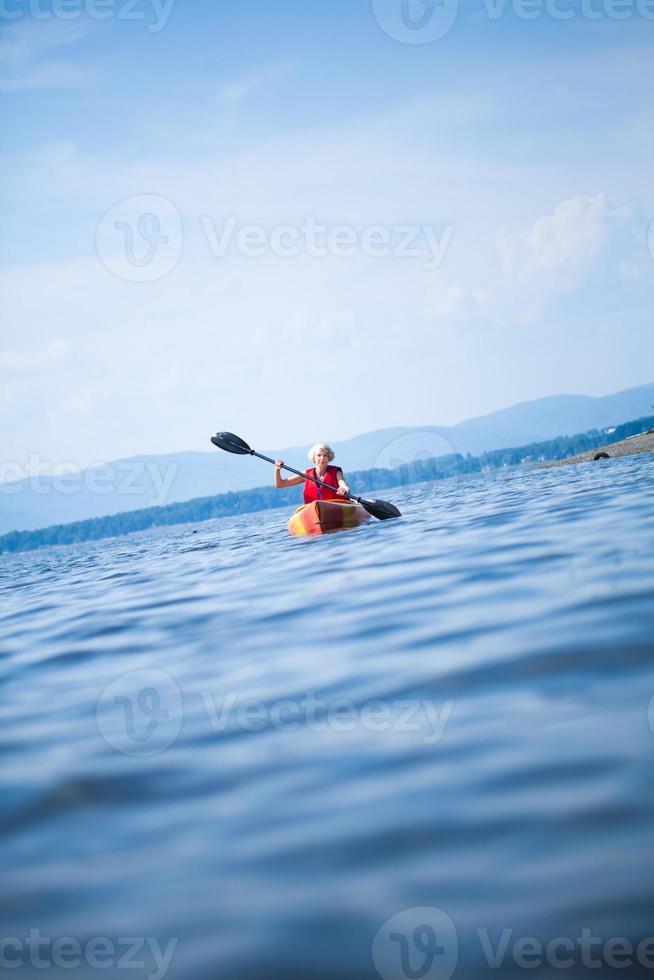 vrouw met veiligheidsvest kajakken alleen op een kalme zee foto
