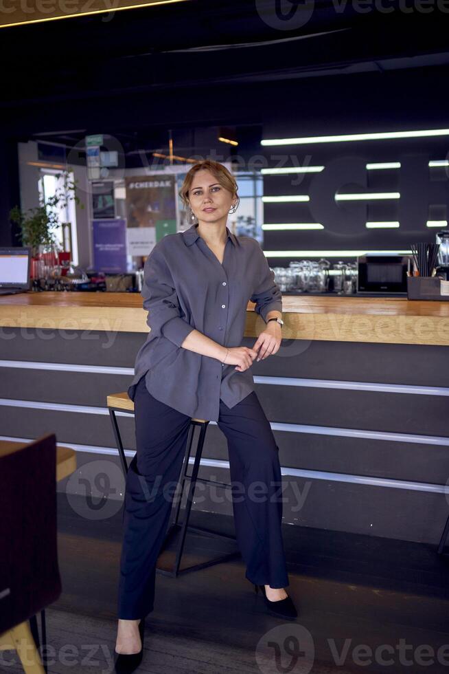 aantrekkelijk midden- leeftijd vrouw in een bar met een neutrale ontwerp, vervelend breed been broek en een zijde blouse foto