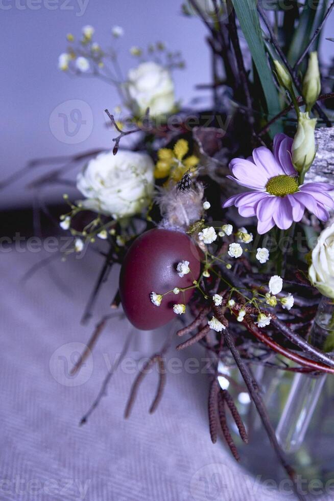 Pasen lauwerkrans, nest van wilg takken en bloemen versierd met eieren en glas test buizen in een transparant vaas foto