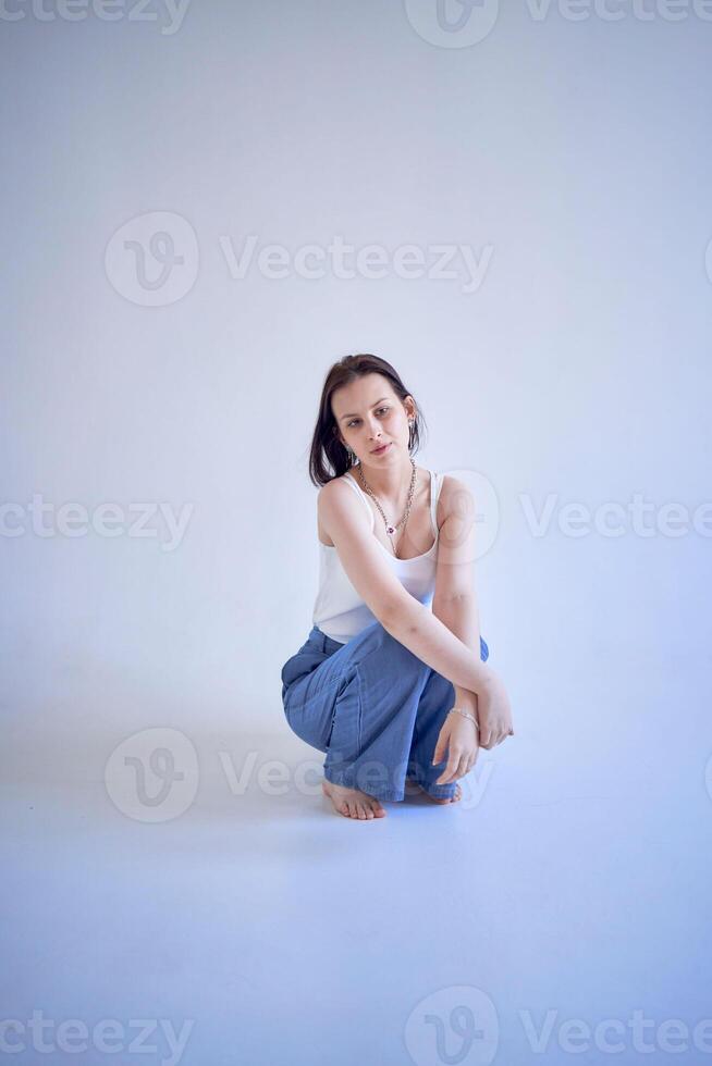 jong tiener- meisje zit Aan een wit cyclorama in de studio foto