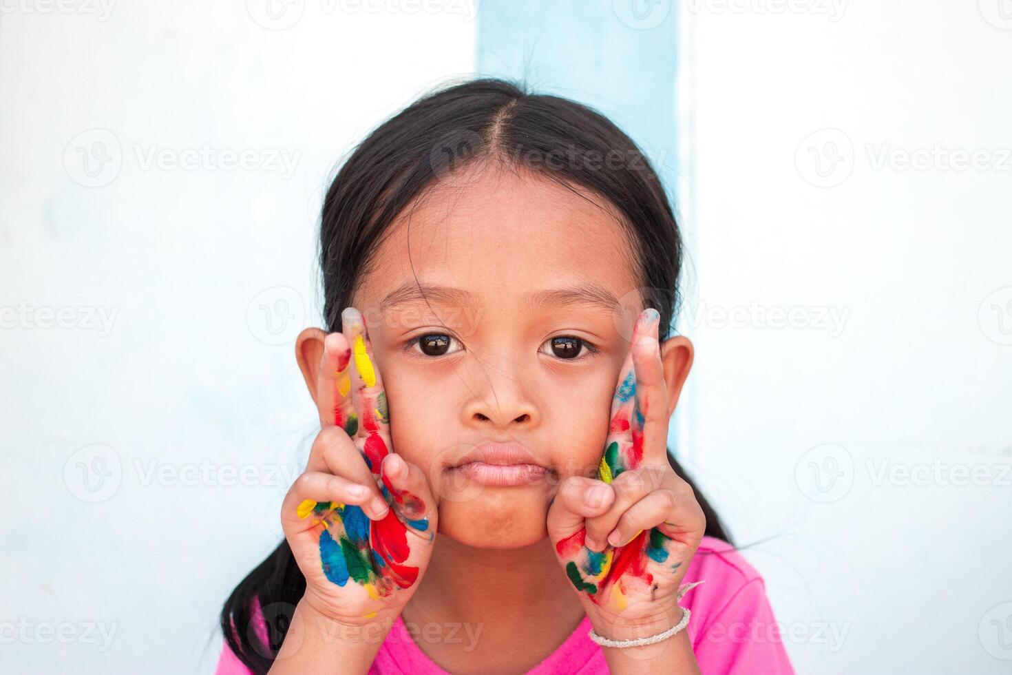 schattig weinig meisje met kleurrijk geschilderd handen Aan muur achtergrond foto