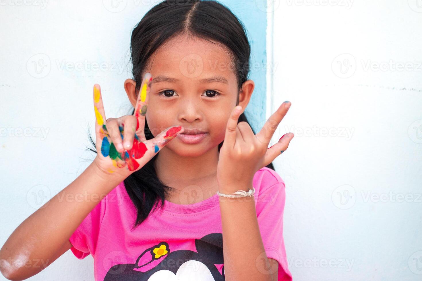 schattig weinig meisje met kleurrijk geschilderd handen Aan muur achtergrond foto