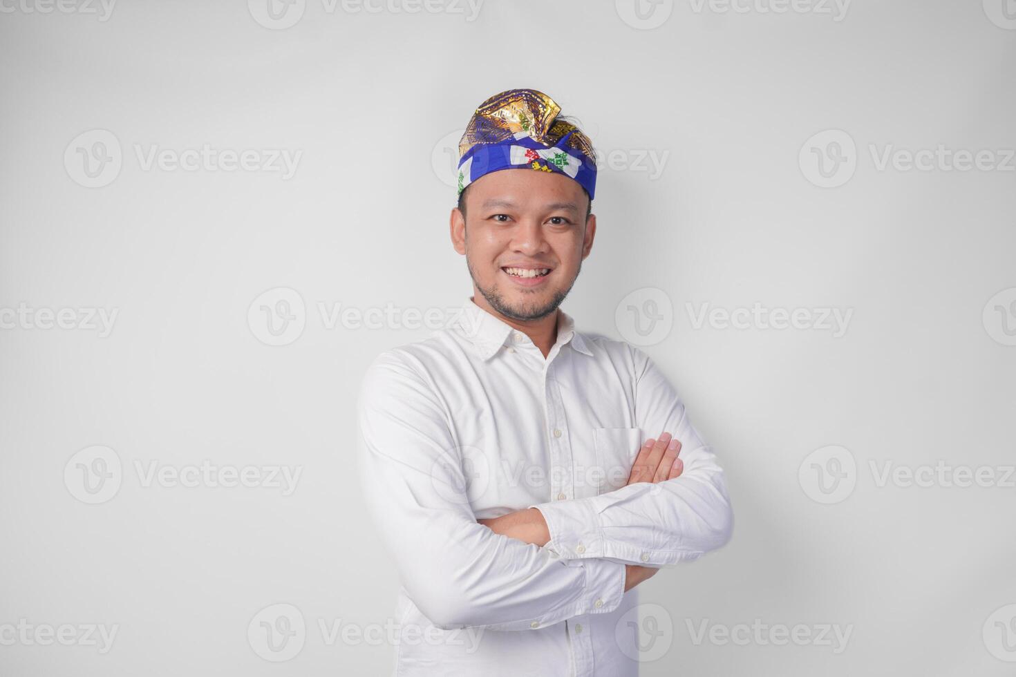 portret van een balinees vervelend traditioneel hoofdtooi gebeld udeng poseren met een gekruiste armen en zelfverzekerd glimlach over- geïsoleerd wit achtergrond foto