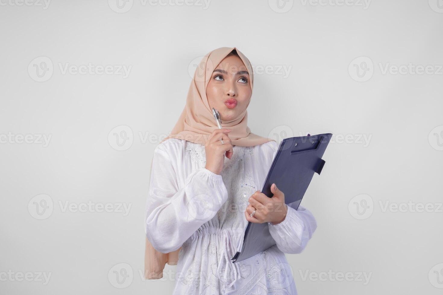 attent jong Aziatisch moslim vrouw vervelend wit jurk en hijab Holding een document, denken terwijl op zoek naar de kopiëren ruimte bovenstaande, geïsoleerd door wit achtergrond. Ramadan en eid mubarak concept foto