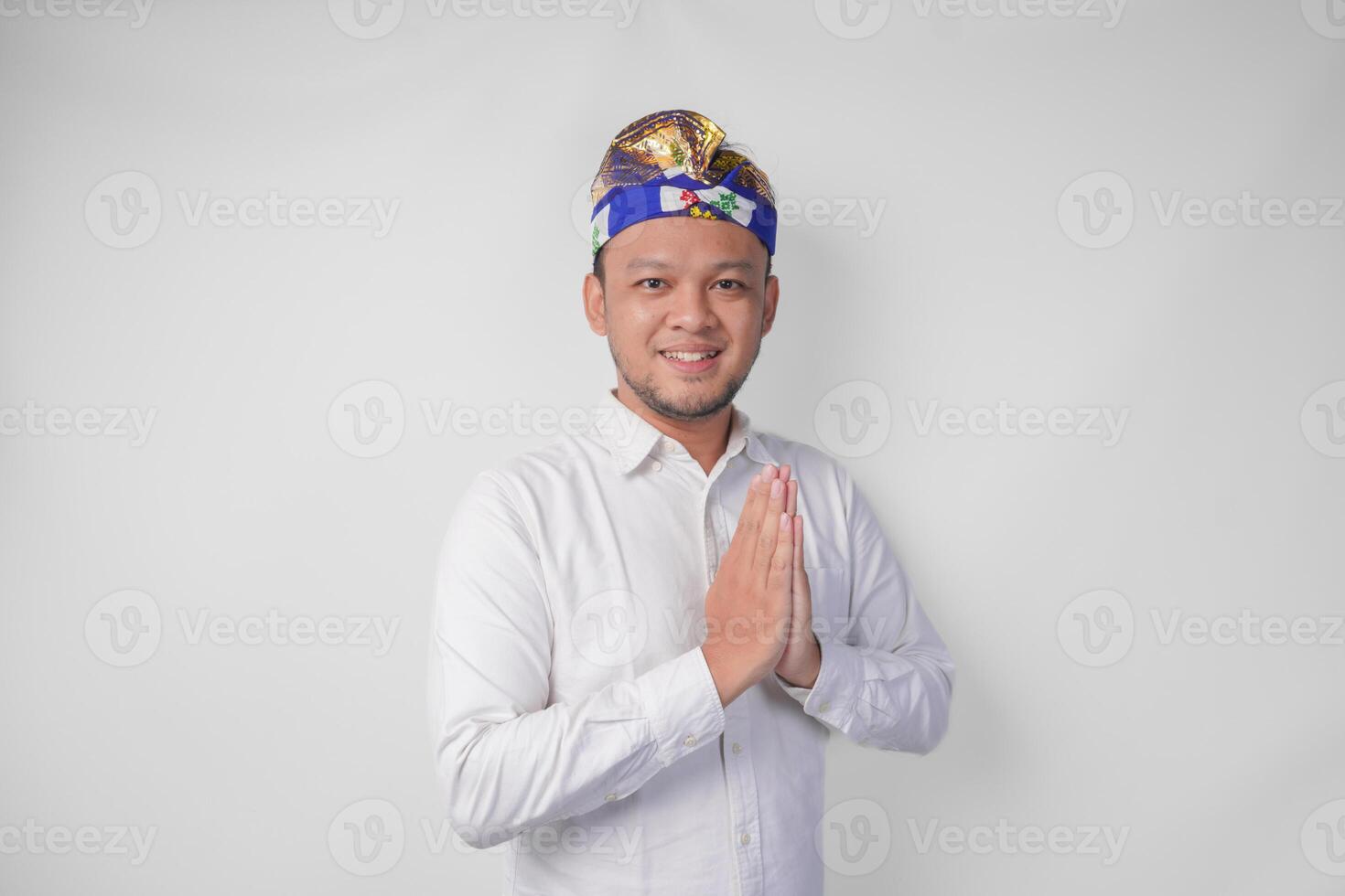 glimlachen jong balinees Mens vervelend traditioneel hoofdtooi gebeld udeng aan het doen groet of Welkom gebaar, geïsoleerd over- wit achtergrond foto