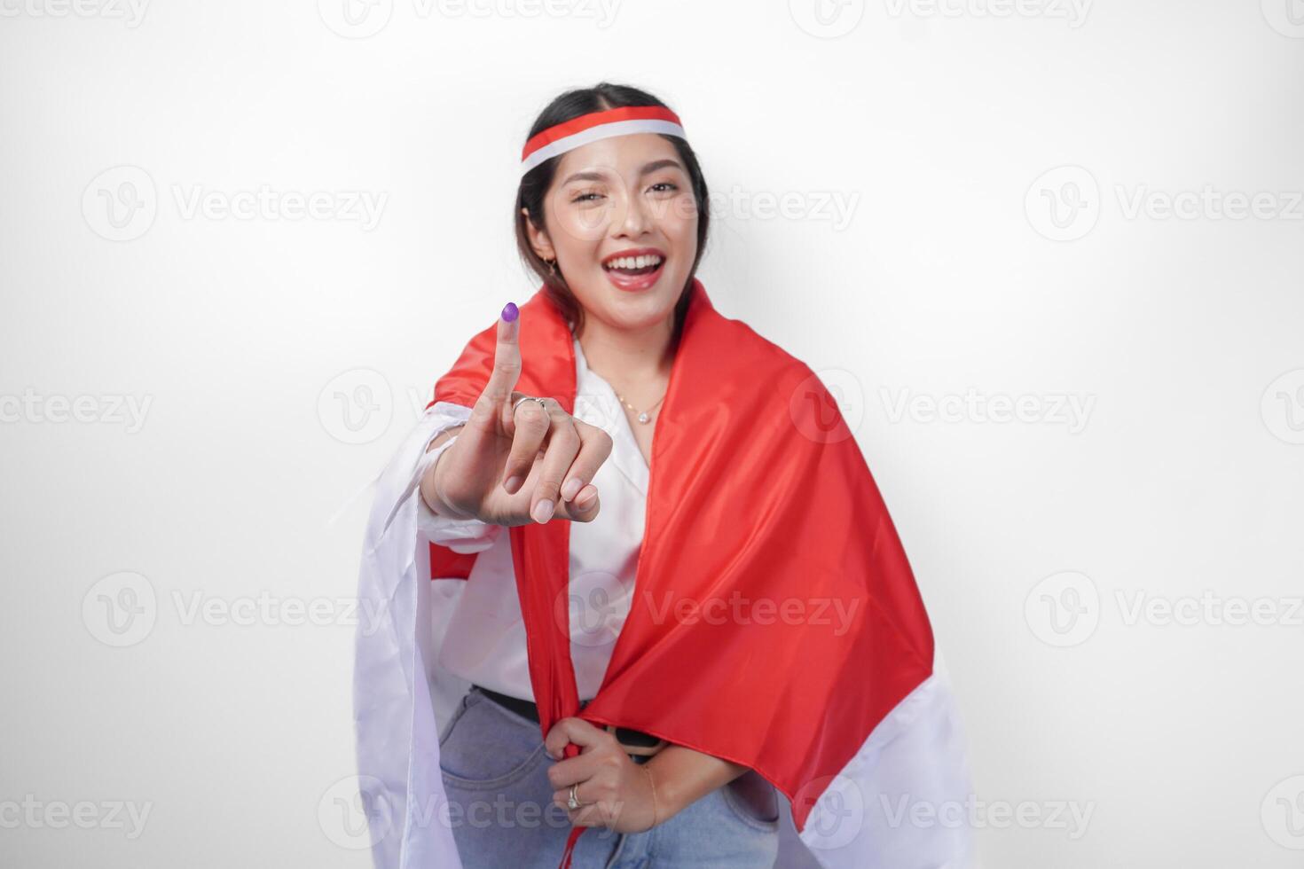 opgewonden Indonesisch vrouw trots tonen weinig vinger gedoopt in Purper inkt na stemmen voor president en parlement verkiezing, vervelend mini vlag hoofdband en wit shirt, aan het bedekken vlag Aan de terug foto